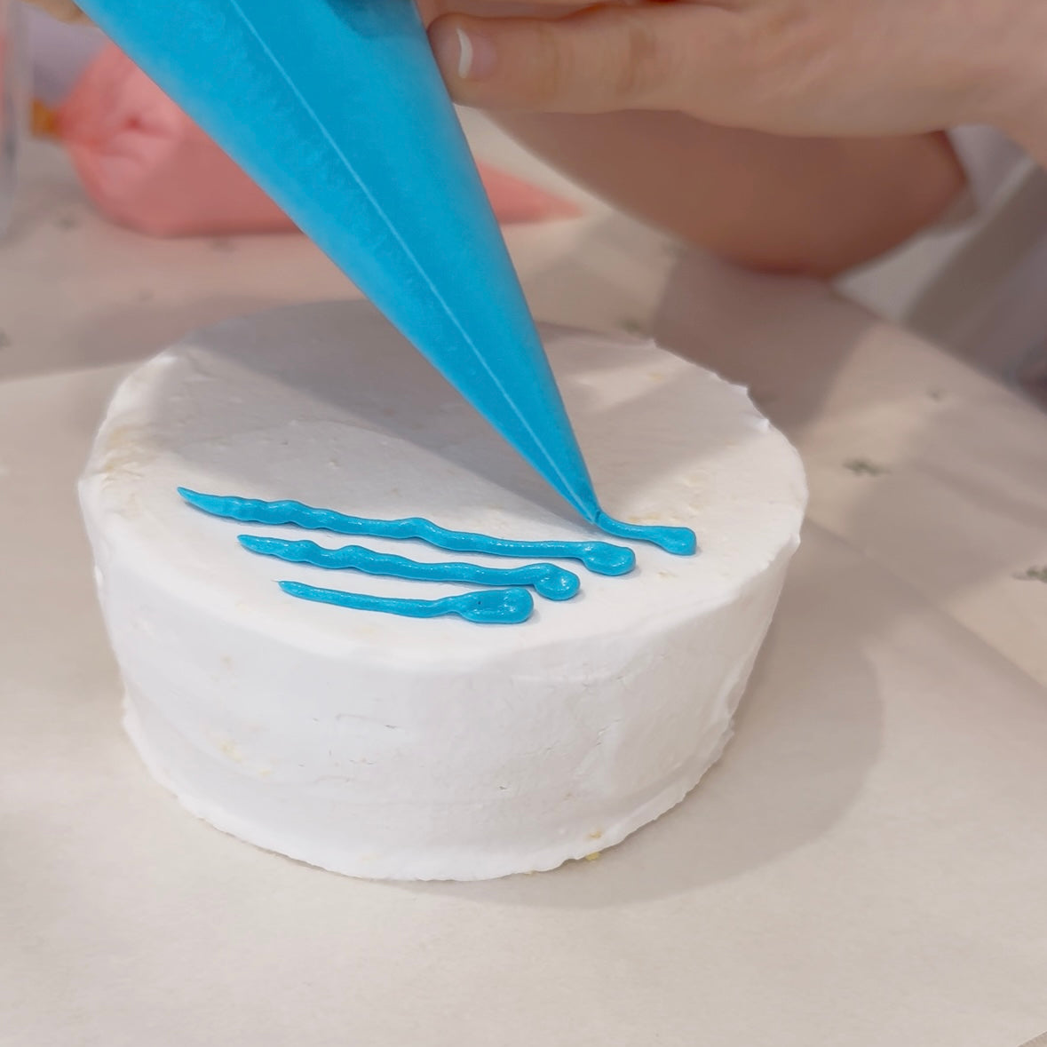 Person decorating a cake with blue icing using a piping bag.
