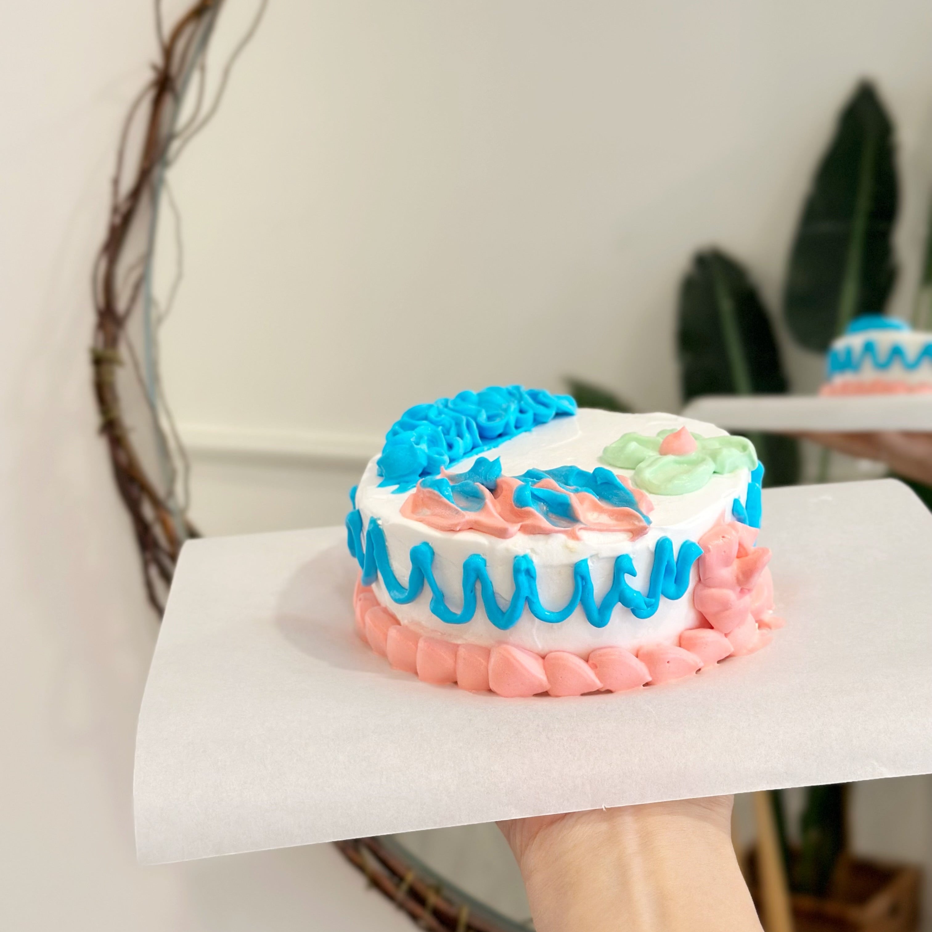 Small cake with pink and blue icing held by a person, with a neutral background