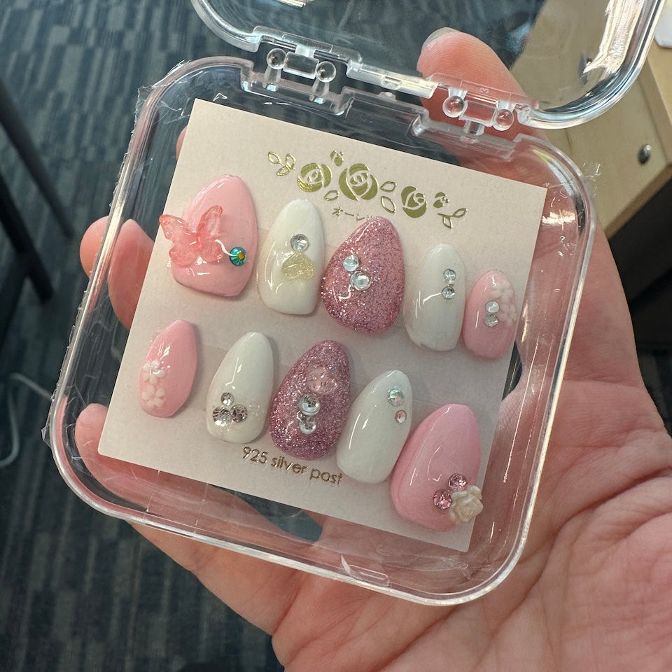 Set of pink and white nail art designs in a clear case held by a hand.