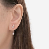 A close-up of a person's ear wearing a delicate rose gold flower stud earring with a dangling clear teardrop crystal.