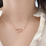 A close-up of a model's neck and chest wearing a delicate rose gold necklace with a butterfly pendant, a small white pearl, and a tiny pink gemstone.