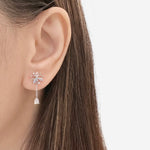 A close-up of a model's ear wearing a silver-toned dangle earring with a butterfly-shaped top and a small clear crystal bell hanging below.