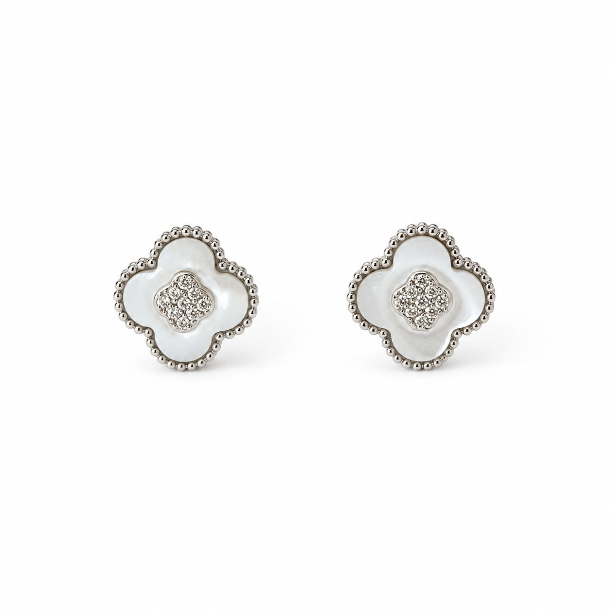 A pair of silver-toned four-leaf clover stud earrings with white inlay and a textured beaded border, set against a plain white background.